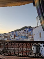 Balcony view at sunset with terracotta rooftops and the sea in the distance.