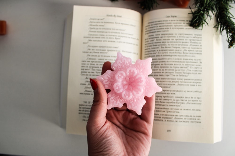 a hand holding a pink flower in front of an open book
