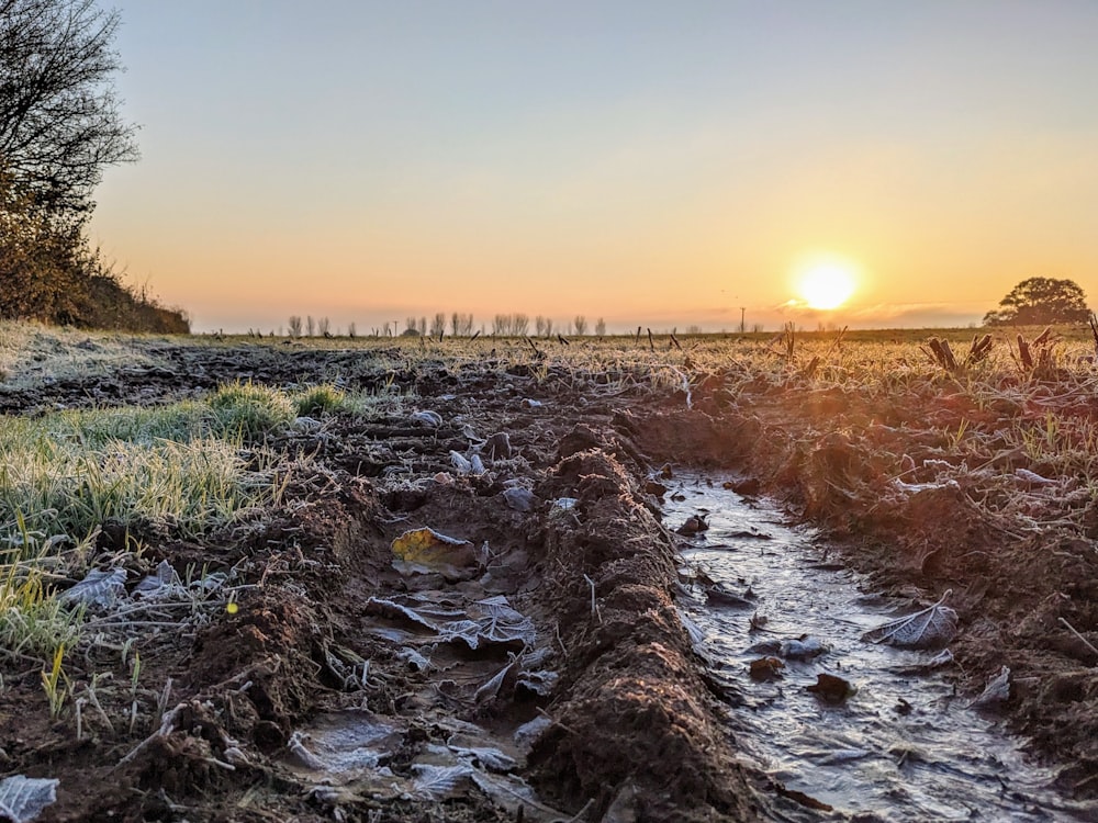 the sun is setting over a muddy field