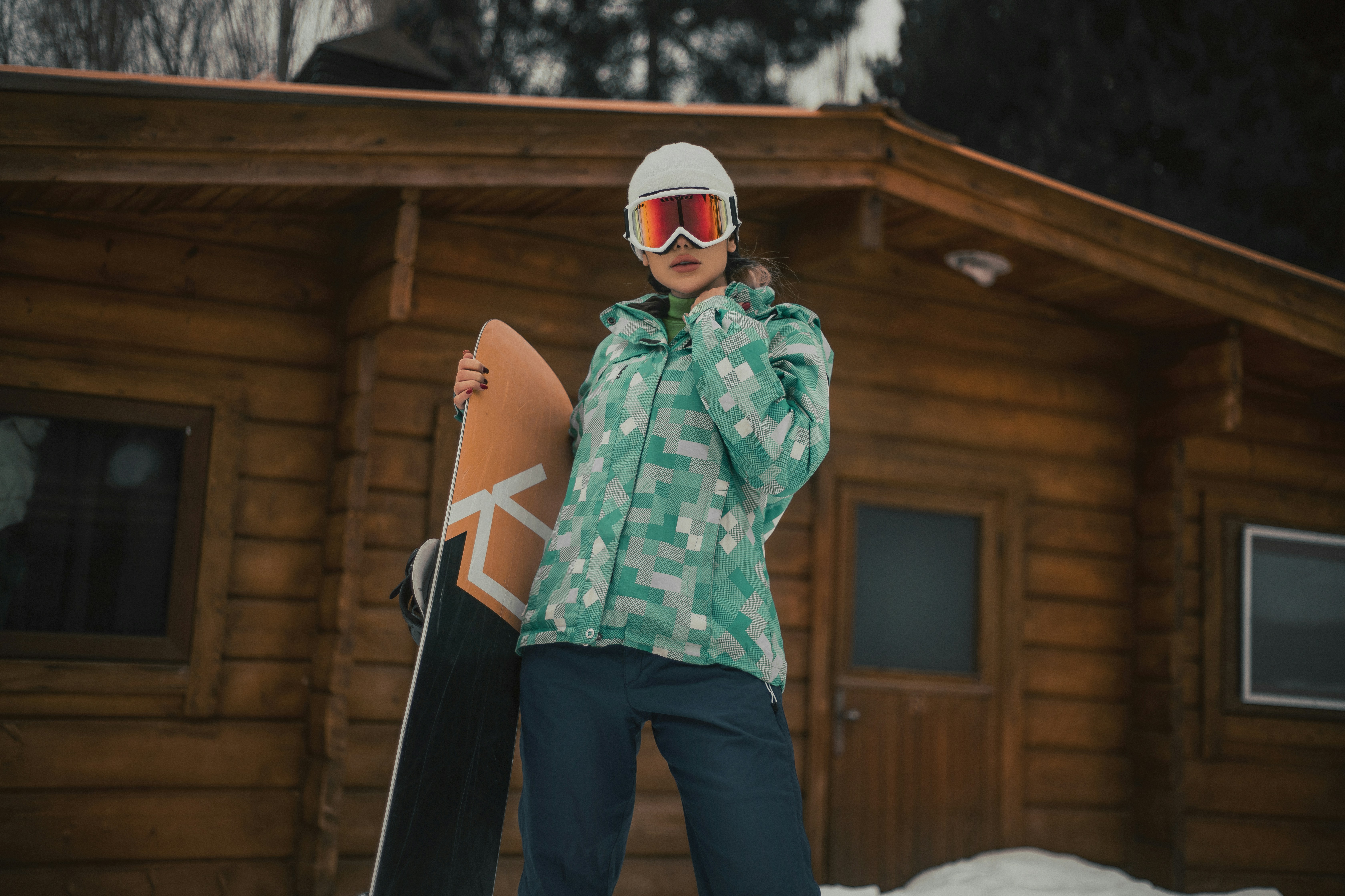 a woman holding a snowboard standing in front of a cabin