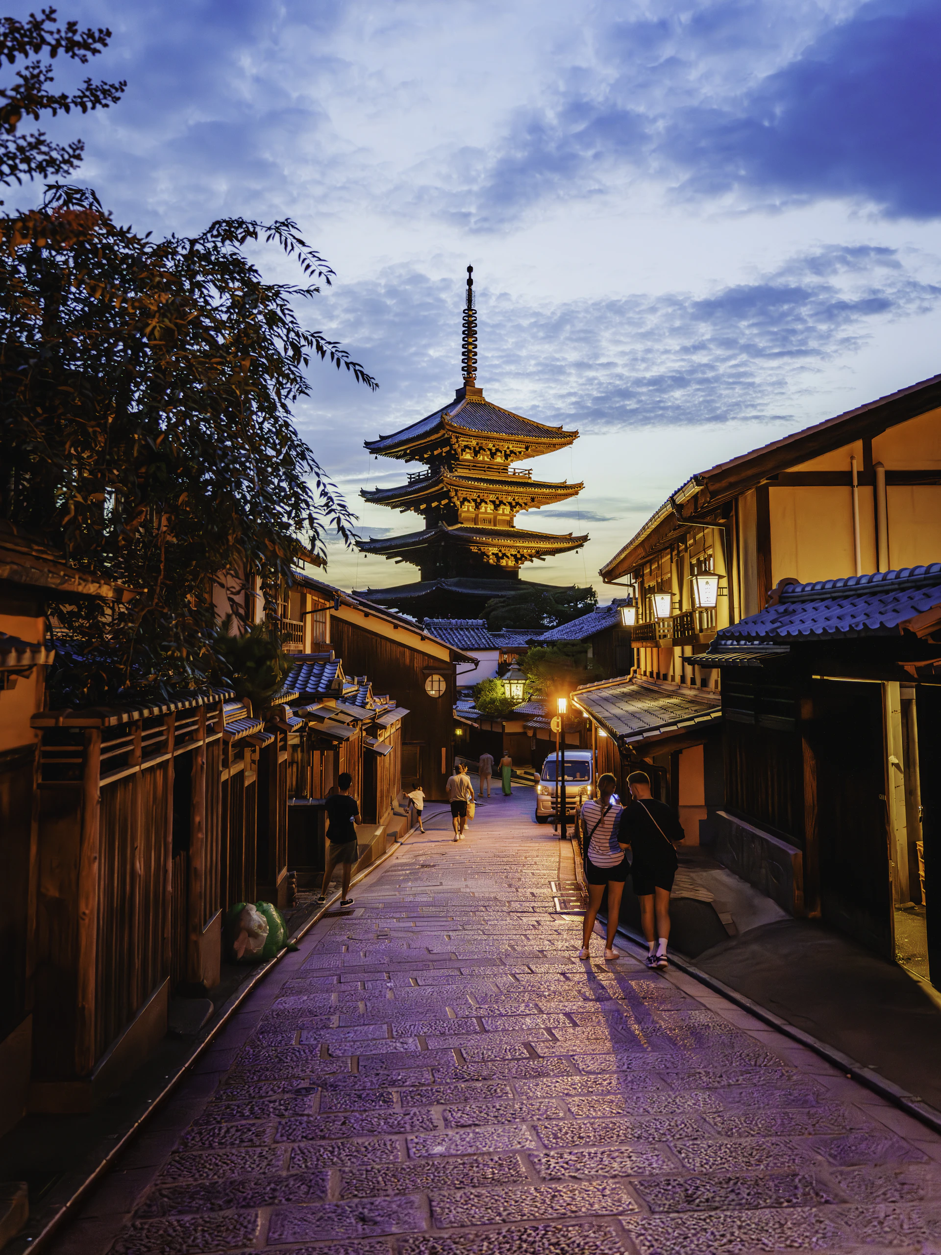 A serene Kyoto temple street at dusk, softly lit with traditional lanterns and cherry blossoms gently falling.