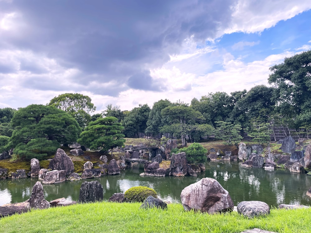 a pond surrounded by rocks and trees under a cloudy sky