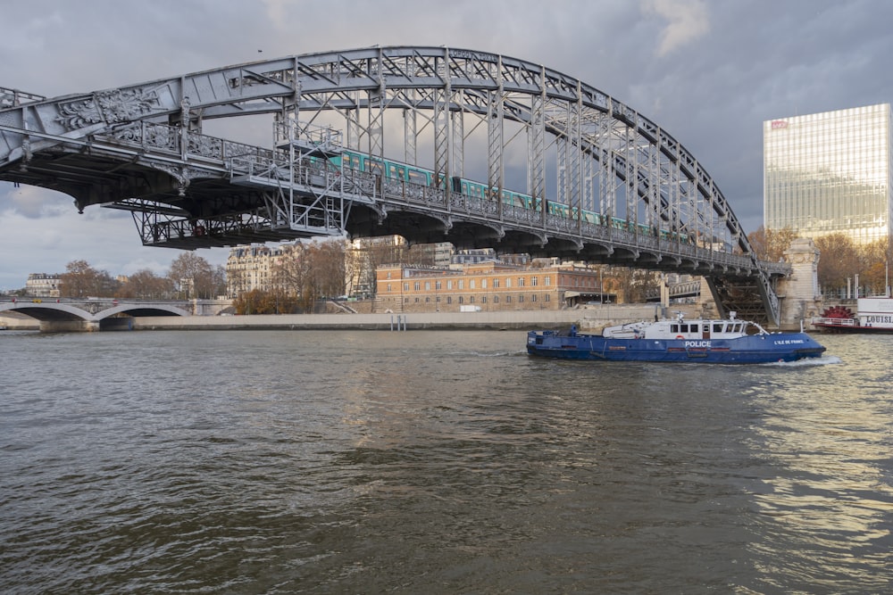 a blue and white boat in the water under a bridge