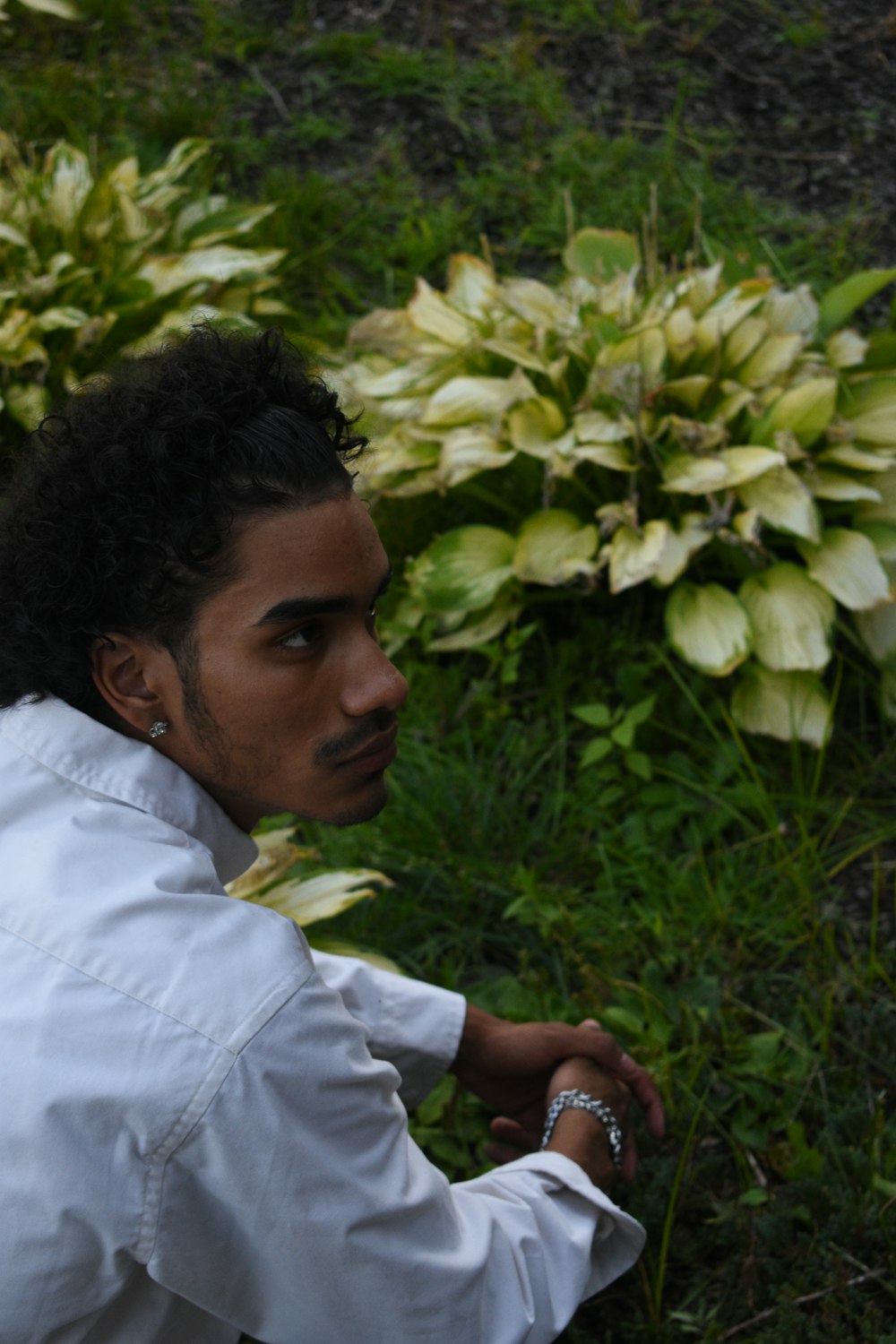 a man in a white shirt and tie sitting in front of a bush