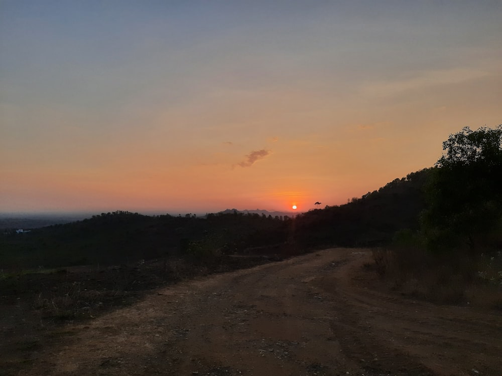 un chemin de terre avec un coucher de soleil en arrière-plan