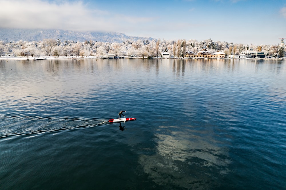 un barco rojo y blanco flotando en la cima de un lago