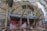 A boat is positioned inside a covered structure, likely for repair or maintenance. The boat has a red and black hull with a white cabin. It is supported by wooden and metal braces, and the covering structure consists of a metal frame with translucent fabric draped over it.