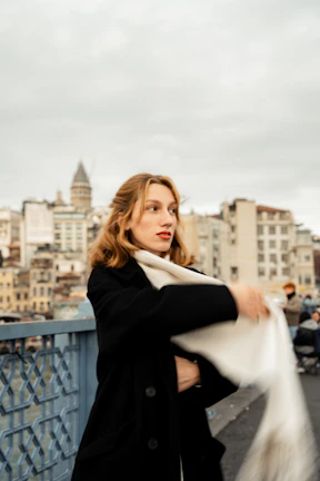 A modern woman wearing a light, elegant scarf wrapped stylishly around her neck on a city street.