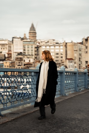 A man wearing a charcoal gray scarf walking through a city street on a breezy day.
