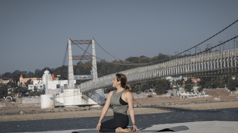 a woman sitting on a yoga mat in front of a bridge