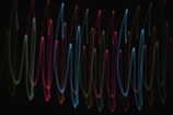 Curving, multicolored light trails move in a repetitive wave pattern against a dark background, creating an abstract visual effect.