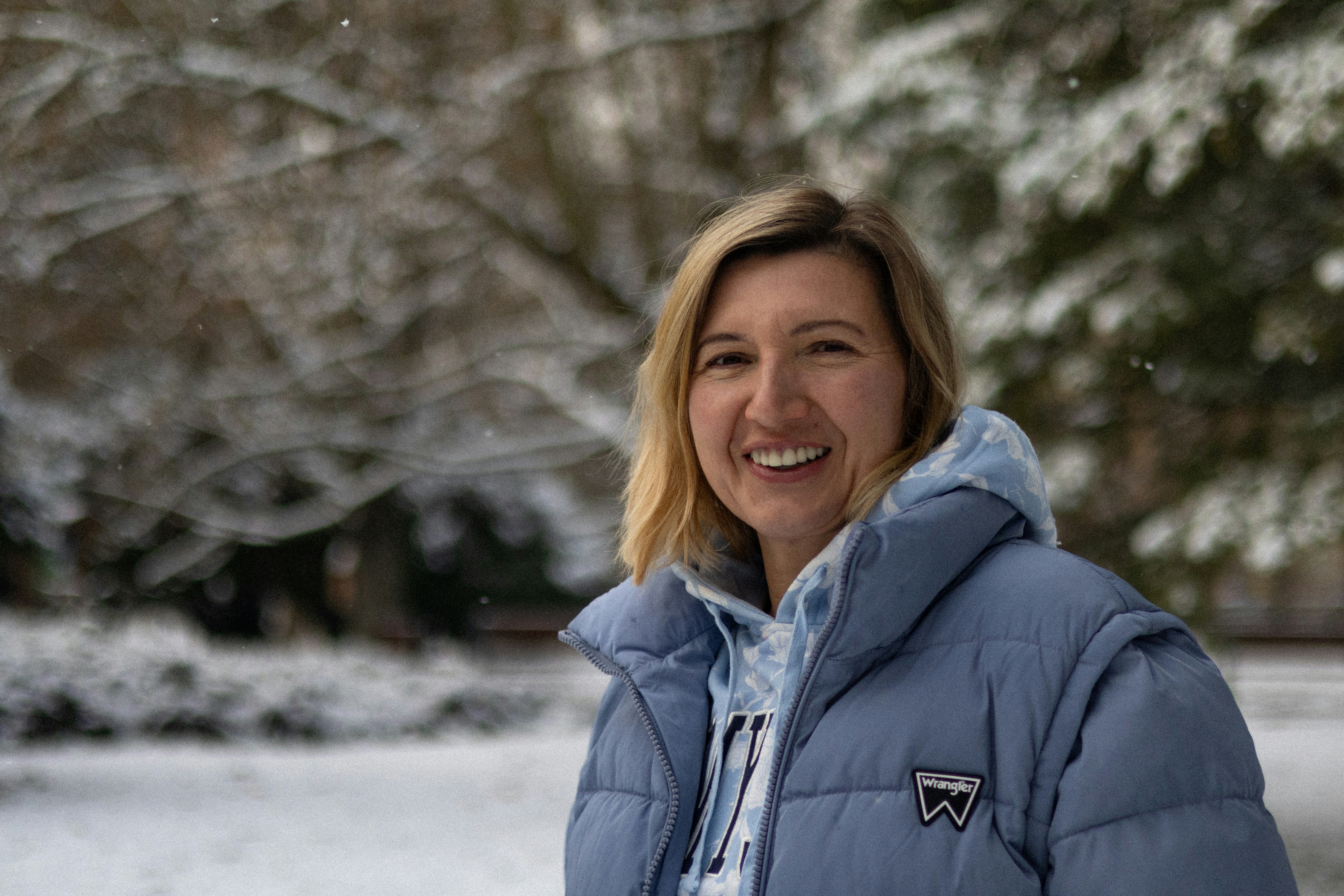 Blonde woman in outdoor jacket against snowy backdrop