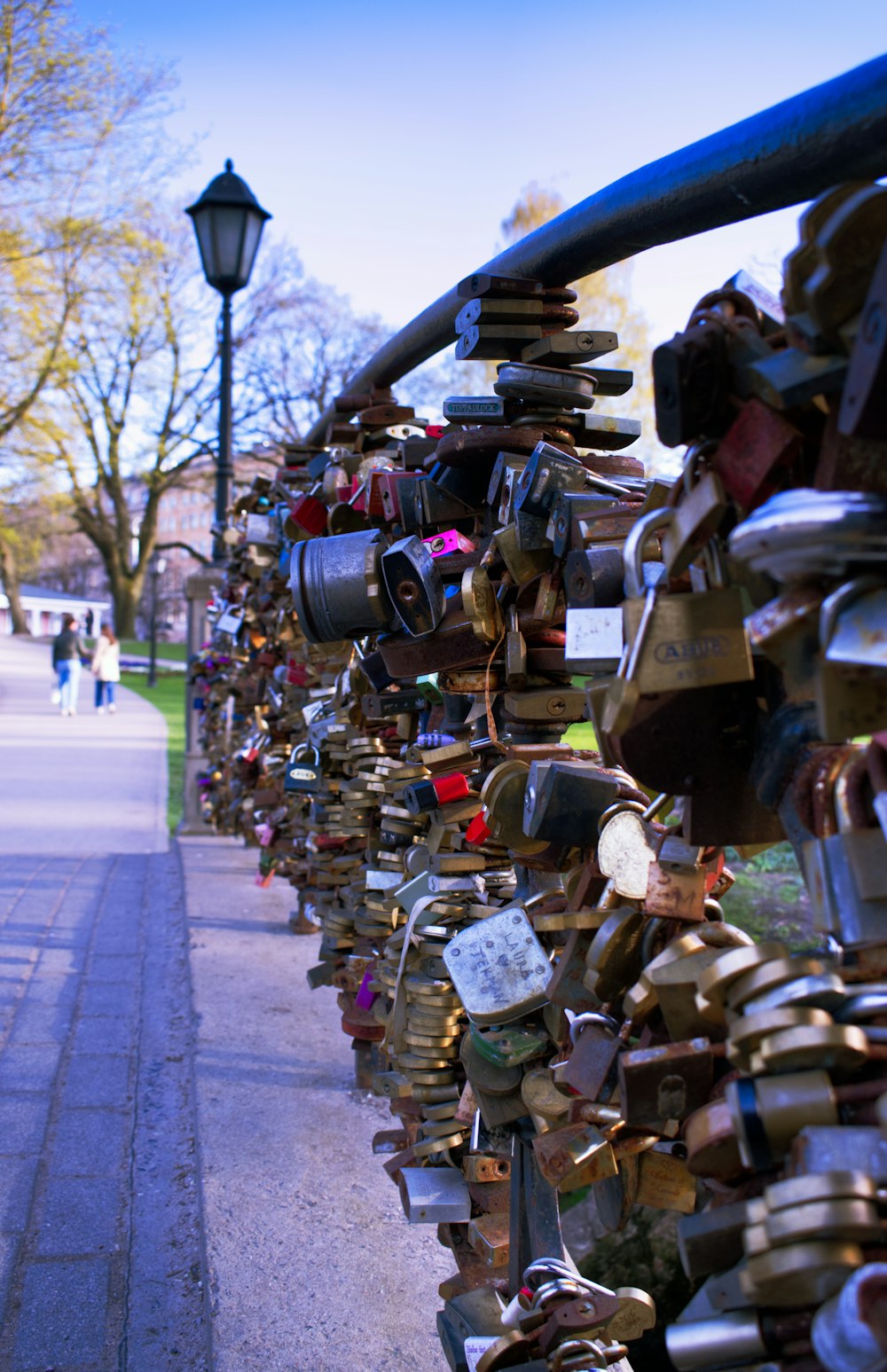 a fence covered in lots of padlocks next to a sidewalk