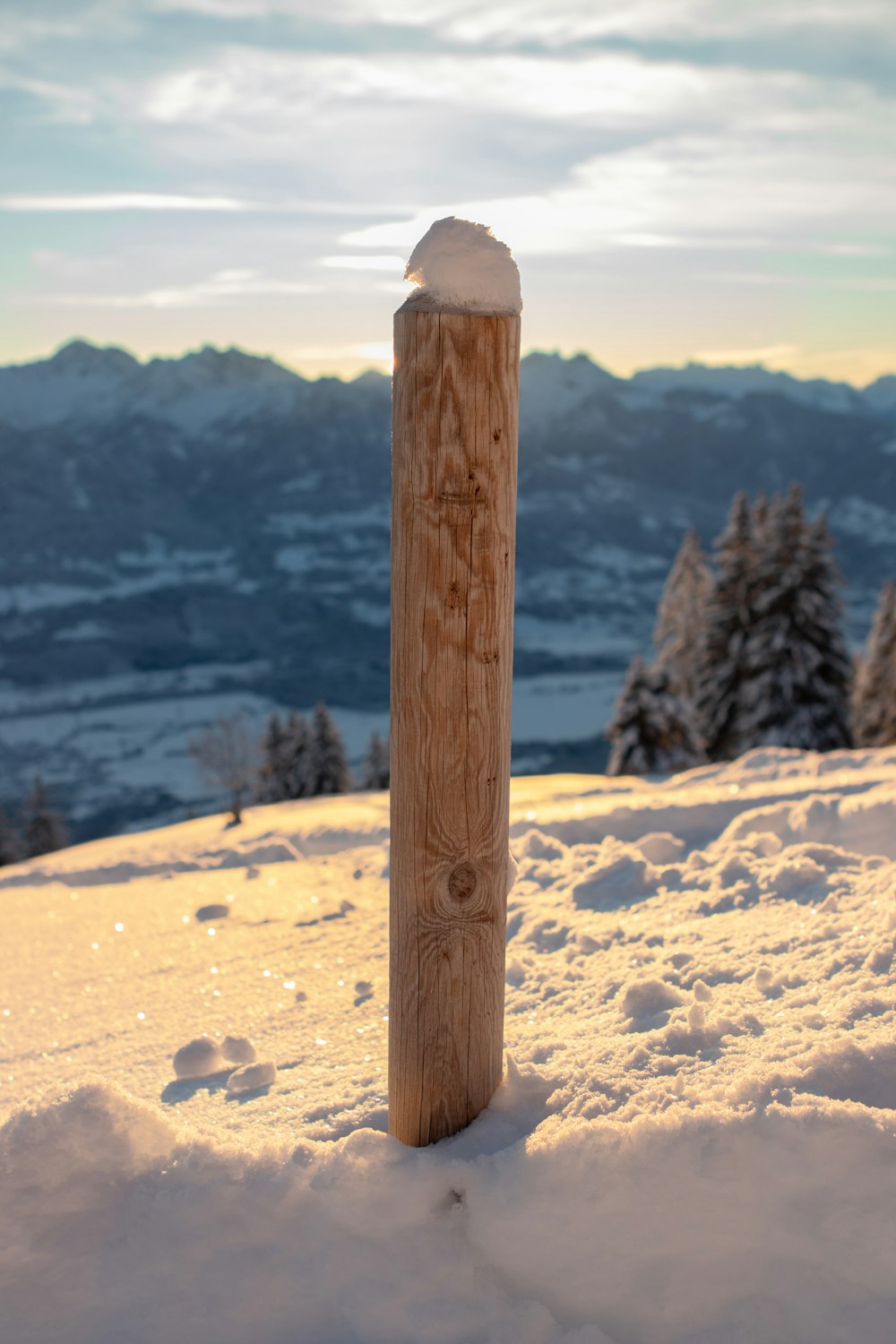a wooden post in the snow with mountains in the background