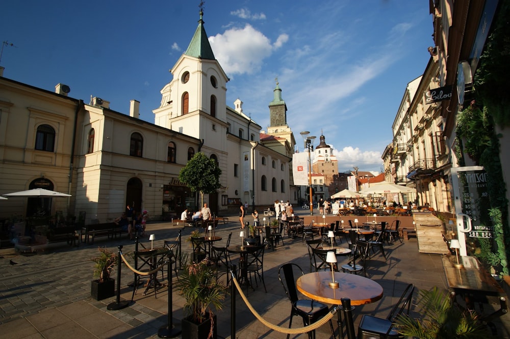 a city square with tables and chairs and a clock tower in the background