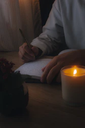 A woman journaling by a window with soft natural light, surrounded by plants.