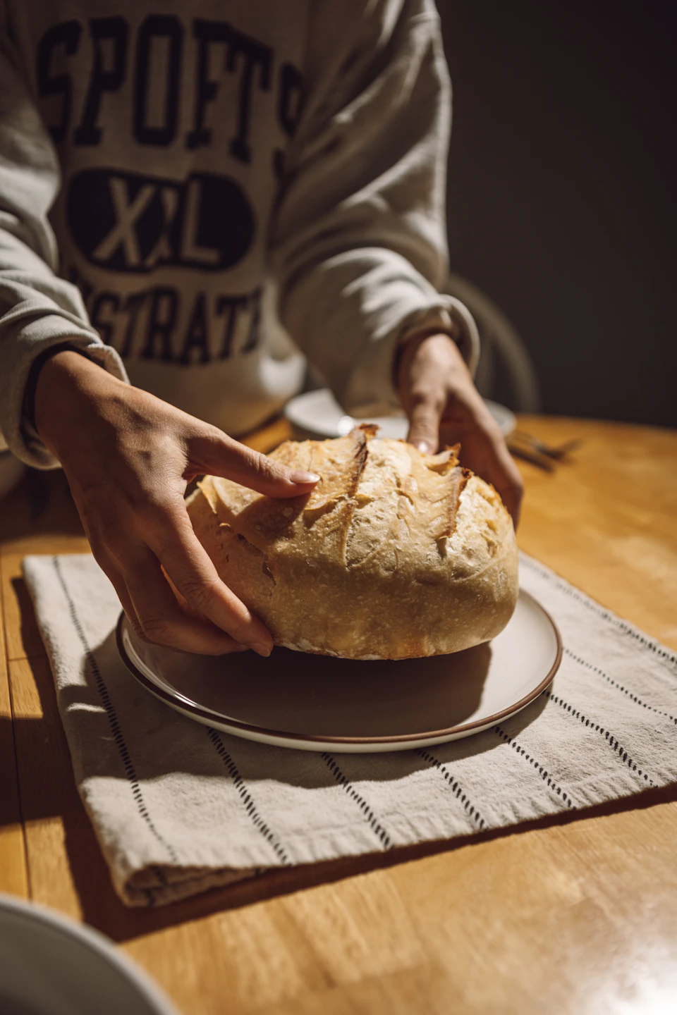 A person's hands hold a large loaf of bread on a wooden table