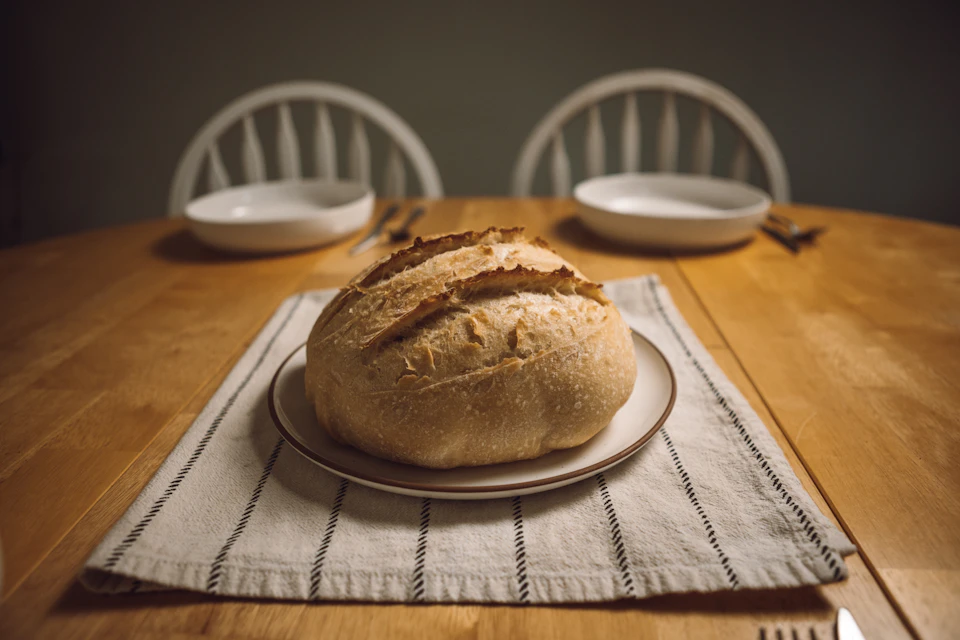 Wooden dining table with two chairs, a loaf of fresh bread on a plate