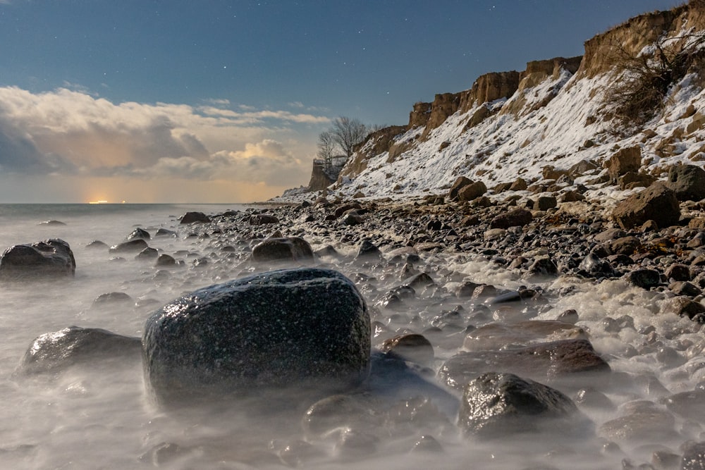 a rocky beach covered in snow under a cloudy sky