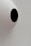 A minimalistic design with a large white semi-spherical dome featuring a single, featureless black oval shape in the center. The background is a plain, light grey color making the black shape stand out starkly against the otherwise neutral tones.