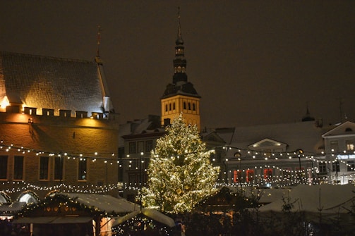 A cozy winter scene of a small town square decorated with Christmas lights and a festive tree.