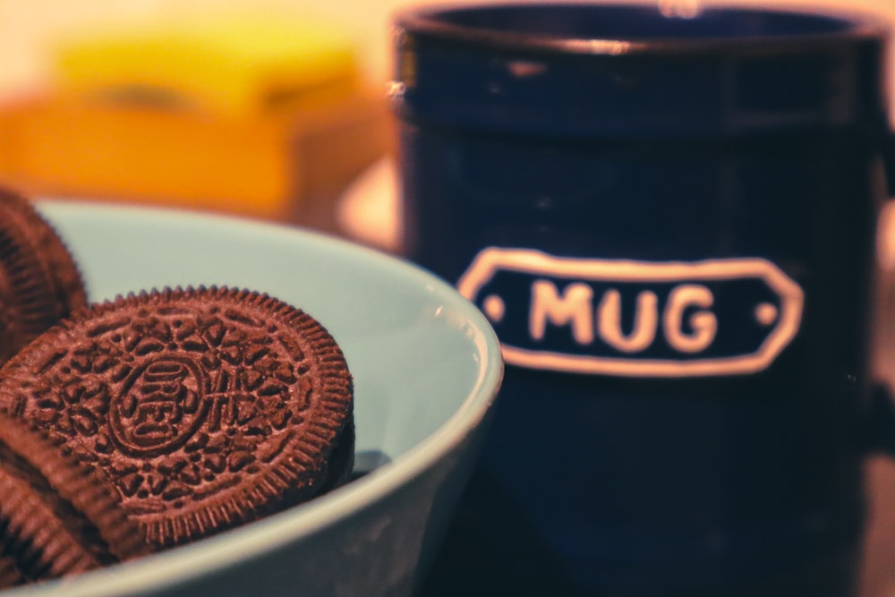 a bowl of chocolate cookies next to a mug