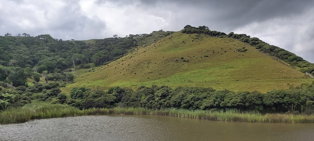 a large green hill with a lake in front of it