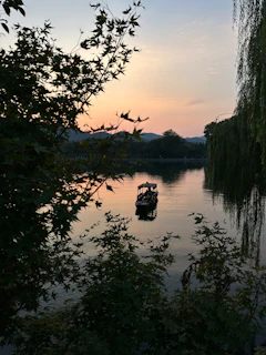 A serene lake view at sunset with a small boat floating gently, framed by mountains.