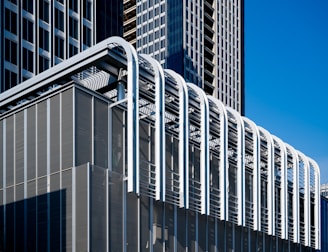 A modern architectural structure featuring sleek lines and a grid-like pattern. The building showcases metal components with a series of vertical and horizontal elements, complemented by large glass windows. The overall design emphasizes a futuristic and industrial aesthetic.