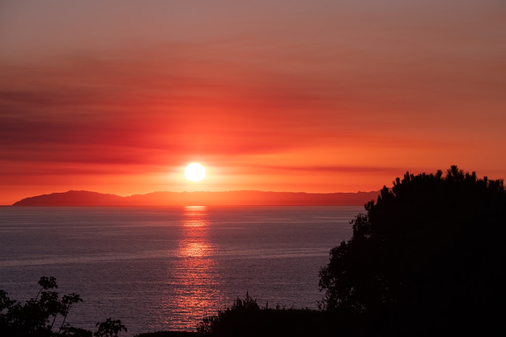 the sun is setting over the ocean with mountains in the background