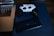 A white and black game controller rests on a blue surface alongside a Nokia smartphone positioned near a laptop. The laptop has a visible keyboard and screen, indicating it's powered on.