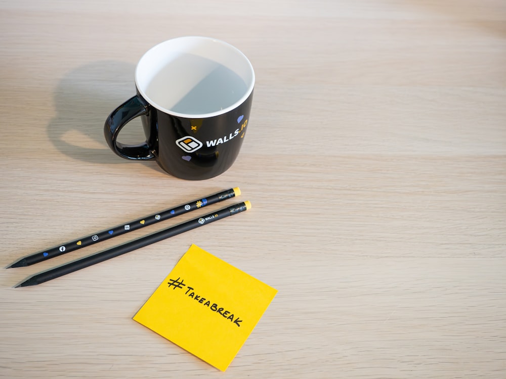 a cup of coffee and two pencils on a table