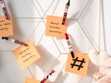 Sticky notes attached with festive-themed clothespins are displayed on a metallic grid, featuring handwritten ideas for holiday marketing campaigns. A small plush heart is also visible.
