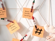 Sticky notes attached with festive-themed clothespins are displayed on a metallic grid, featuring handwritten ideas for holiday marketing campaigns. A small plush heart is also visible.
