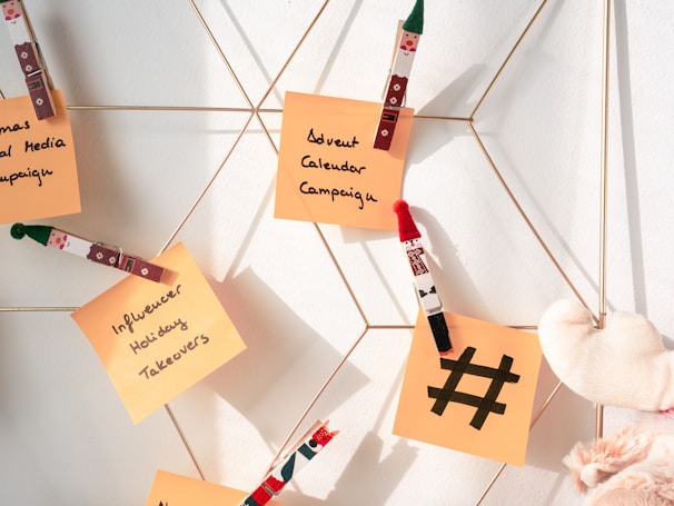 Sticky notes attached with festive-themed clothespins are displayed on a metallic grid, featuring handwritten ideas for holiday marketing campaigns. A small plush heart is also visible.