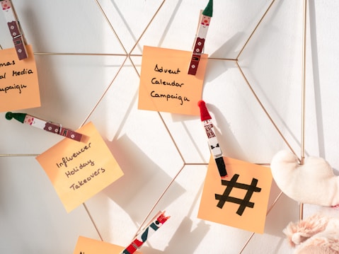 Sticky notes attached with festive-themed clothespins are displayed on a metallic grid, featuring handwritten ideas for holiday marketing campaigns. A small plush heart is also visible.