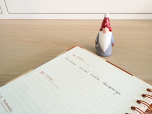 A planner opened to a page for Monday, the 9th, with a note reading 'Christmas Social Media Campaign.' A small decorative Santa figure is positioned on a wooden desk surface beside the planner.