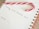 A candy cane rests on an open spiral notebook with an entry titled 'Holiday Email Marketing Series' written on it. The notebook page is white with lined sections, and the spiral binding is brown.