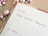 A planner or calendar is open to Monday, the 16th, with the words 'Advent Calendar Campaign' written in black ink. Surrounding the planner are shiny, metallic Christmas ornaments in shades of pink and silver. The planner has a wooden table underneath.
