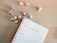 A spiral-bound notebook is open on a wooden surface, displaying a page with handwritten text that reads 'Influencer Holiday Takeovers.' Pink ornaments, resembling Christmas baubles, are scattered around the notebook, creating a festive atmosphere.