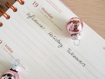 A calendar page open to Thursday the 19th with handwritten notes reading 'Influencer Holiday Takeovers.' The page is decorated with two small pink Christmas ornaments.