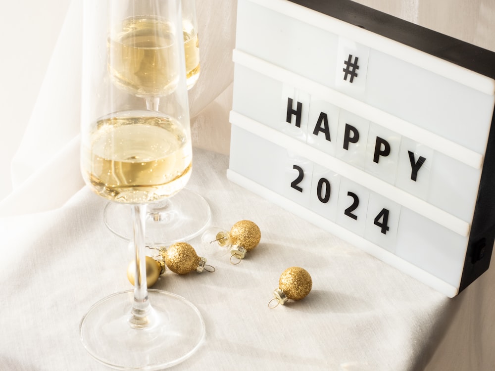 a glass of white wine next to a happy new year sign