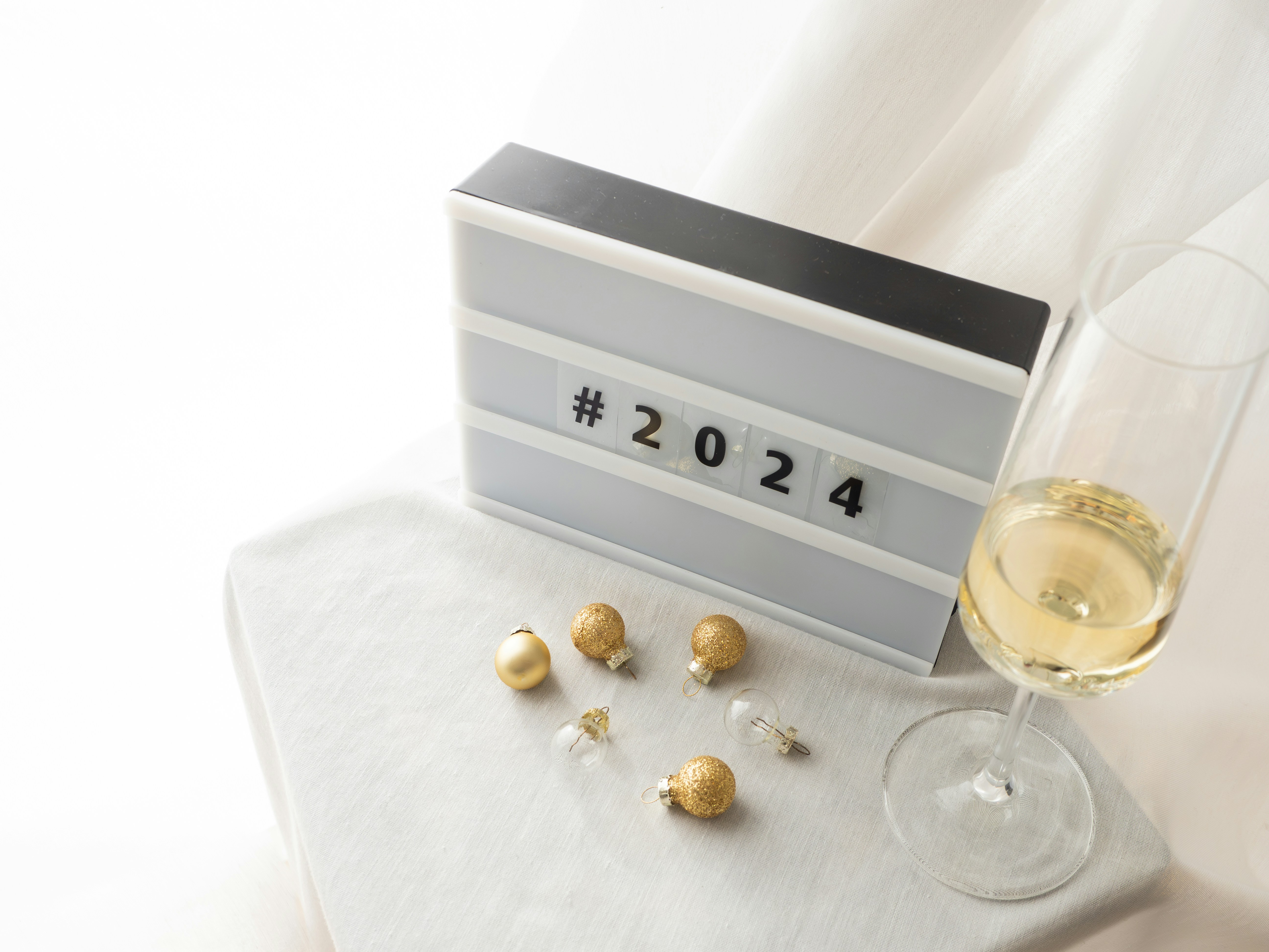 Festive decorations with champagne glasses on a white background and a lightbox with the hashtag #2024