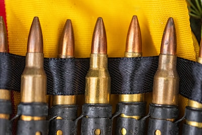 Several bullets are neatly aligned in a black belt against a background of yellow fabric. The bullets have a brass casing with copper-colored tips, and the black belt holds them securely in place.