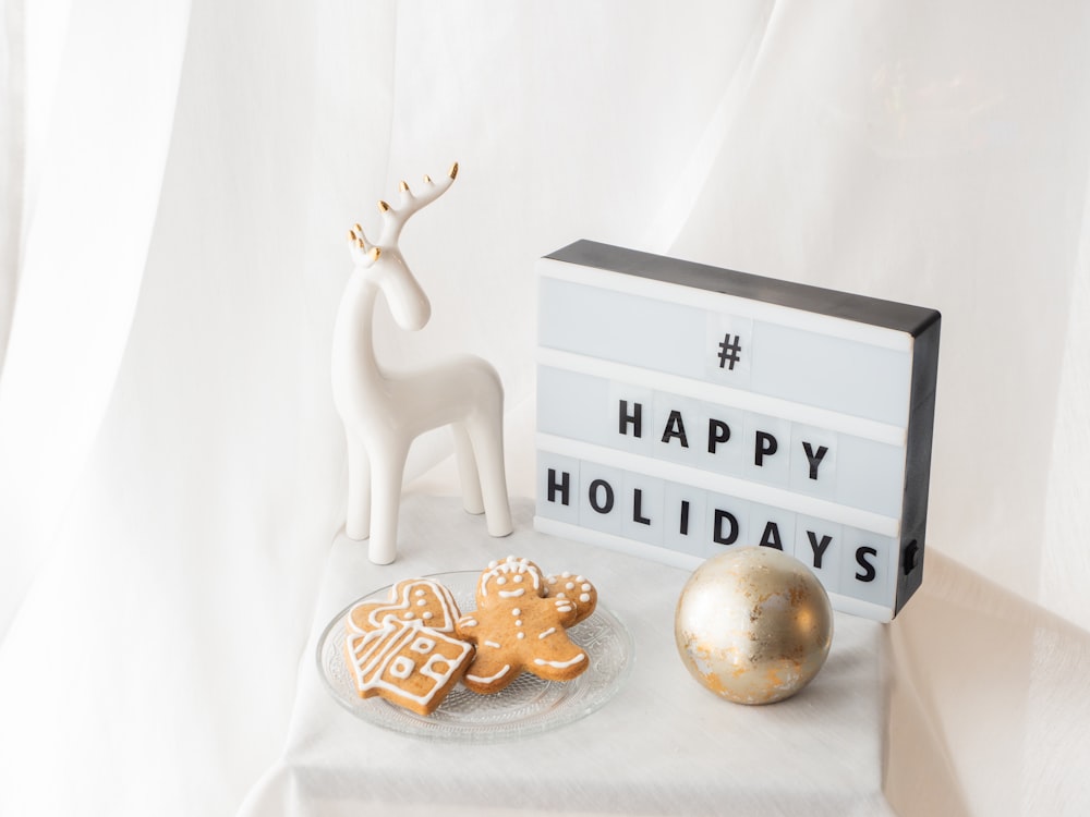 a white reindeer figurine next to a happy holidays sign