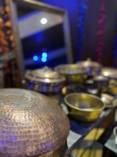 A beautifully arranged set of copper thali plates and glasses glowing under warm light on a dark background.