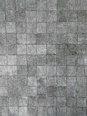 A pattern of small, square tiles with a textured, stone-like appearance, arranged in a grid pattern.