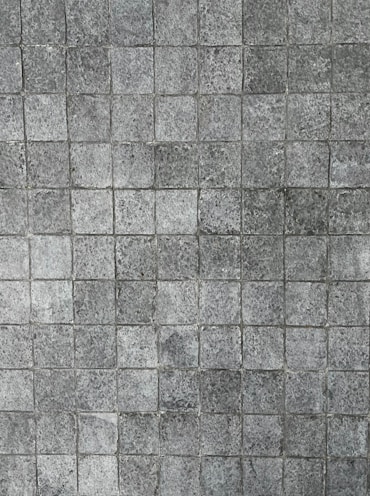 A pattern of small, square tiles with a textured, stone-like appearance, arranged in a grid pattern.