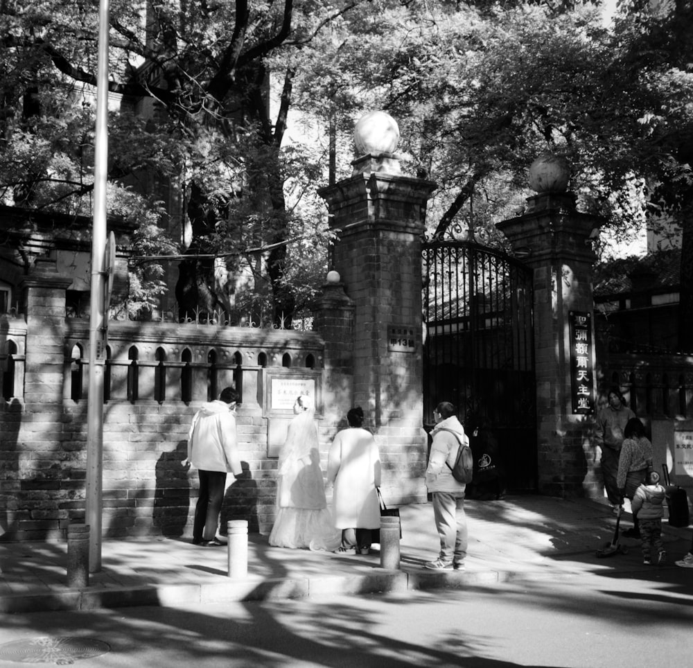 a black and white photo of people walking in front of a gate