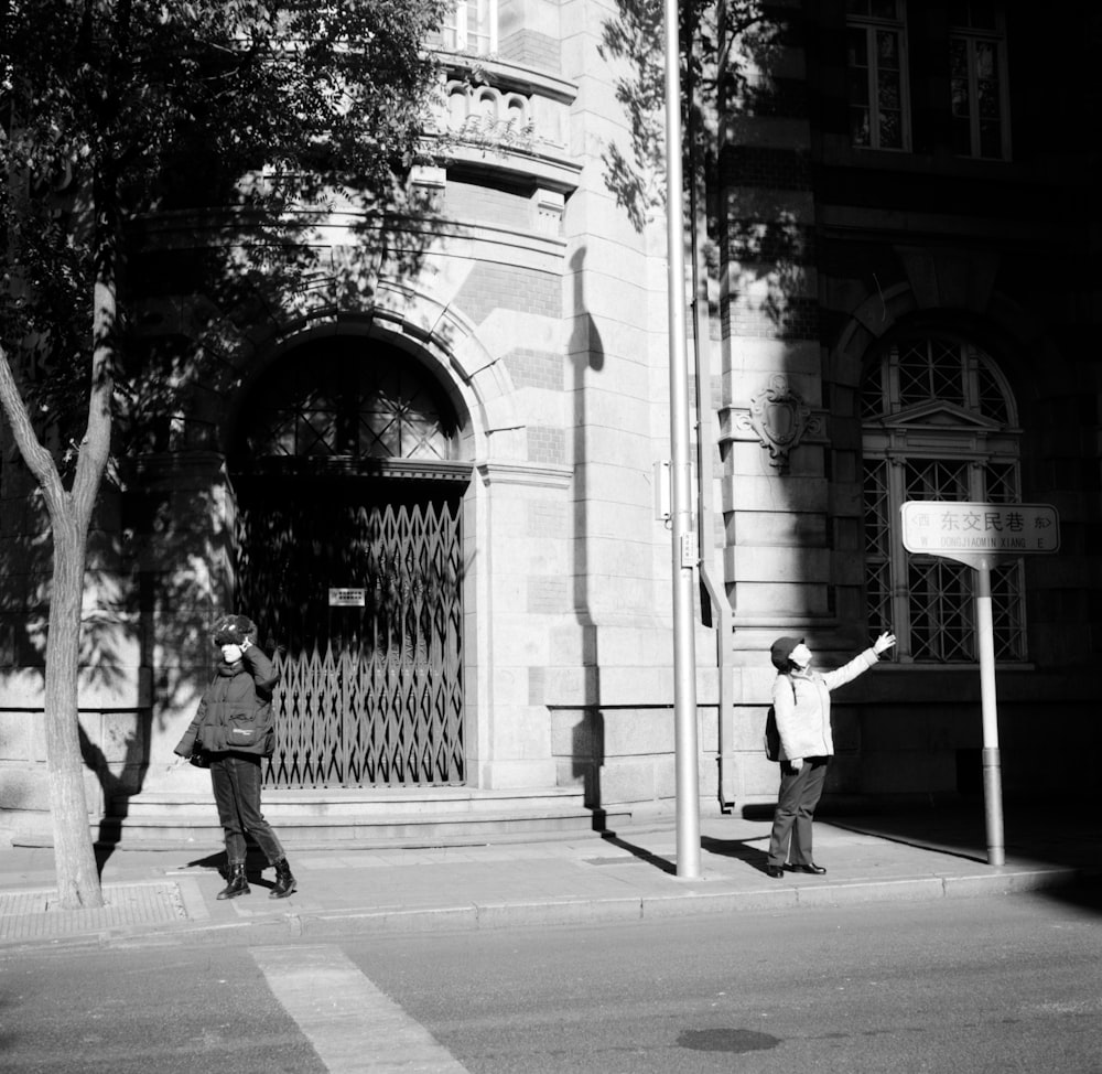 a black and white photo of two people on a street corner